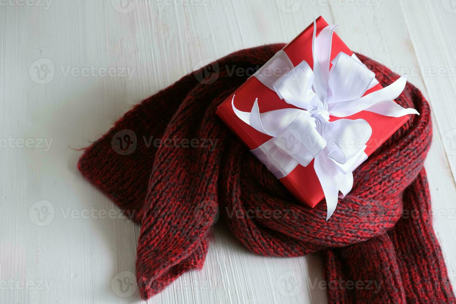 Red gift box isolated on a red knitted scarf with white wooden background with. Christmas's day concept. Planning scheduling agenda, Event, organiser x'mas day. Flat lay, top view. photo