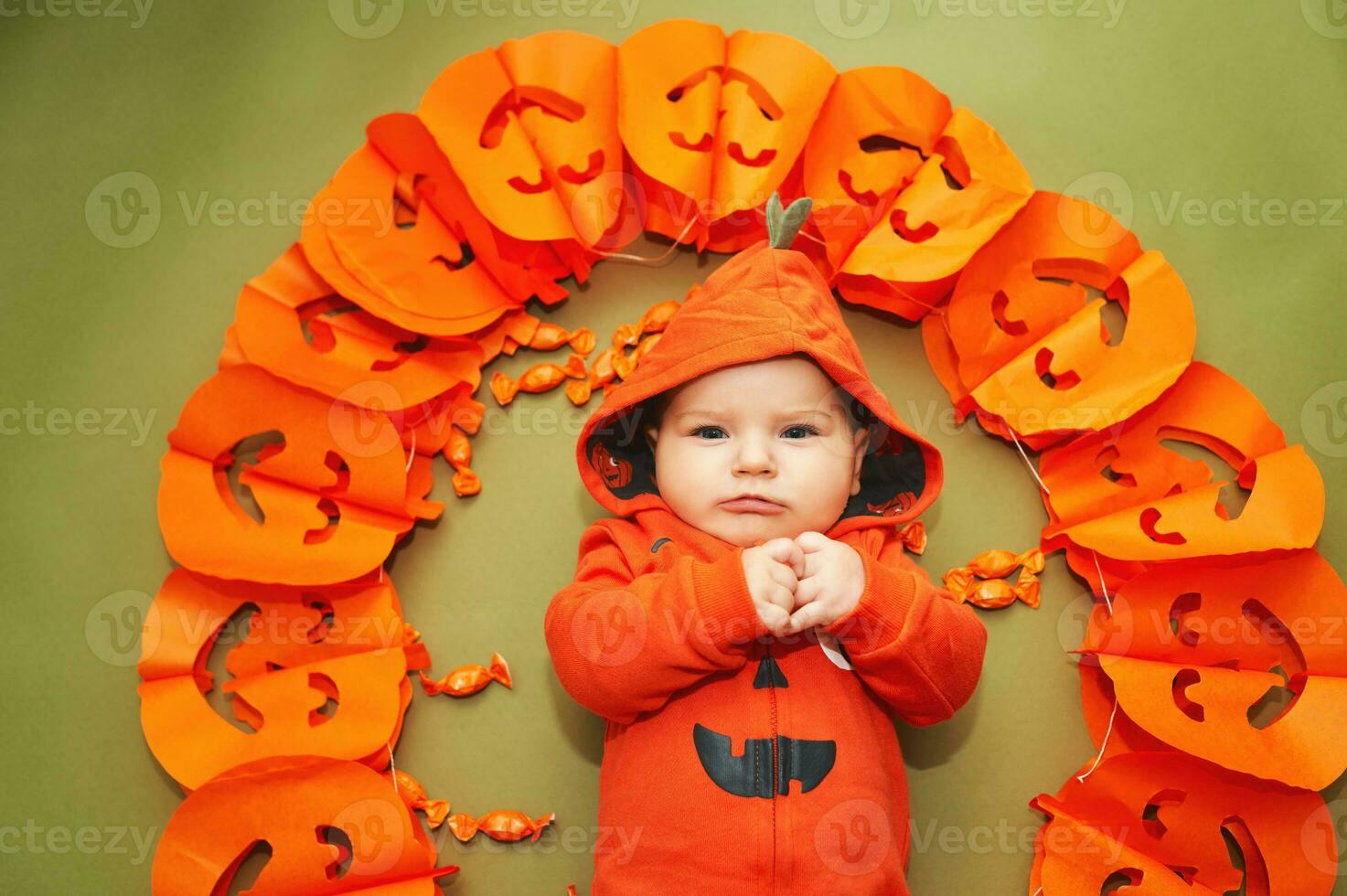 Halloween portrait of adorable baby lying on green background next to pumpkin garland photo