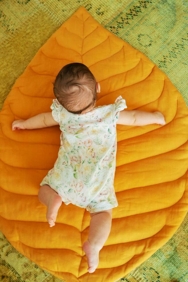 Portrait of adorable 6 months old baby lying on yellow play blanket, back view, belly time training photo