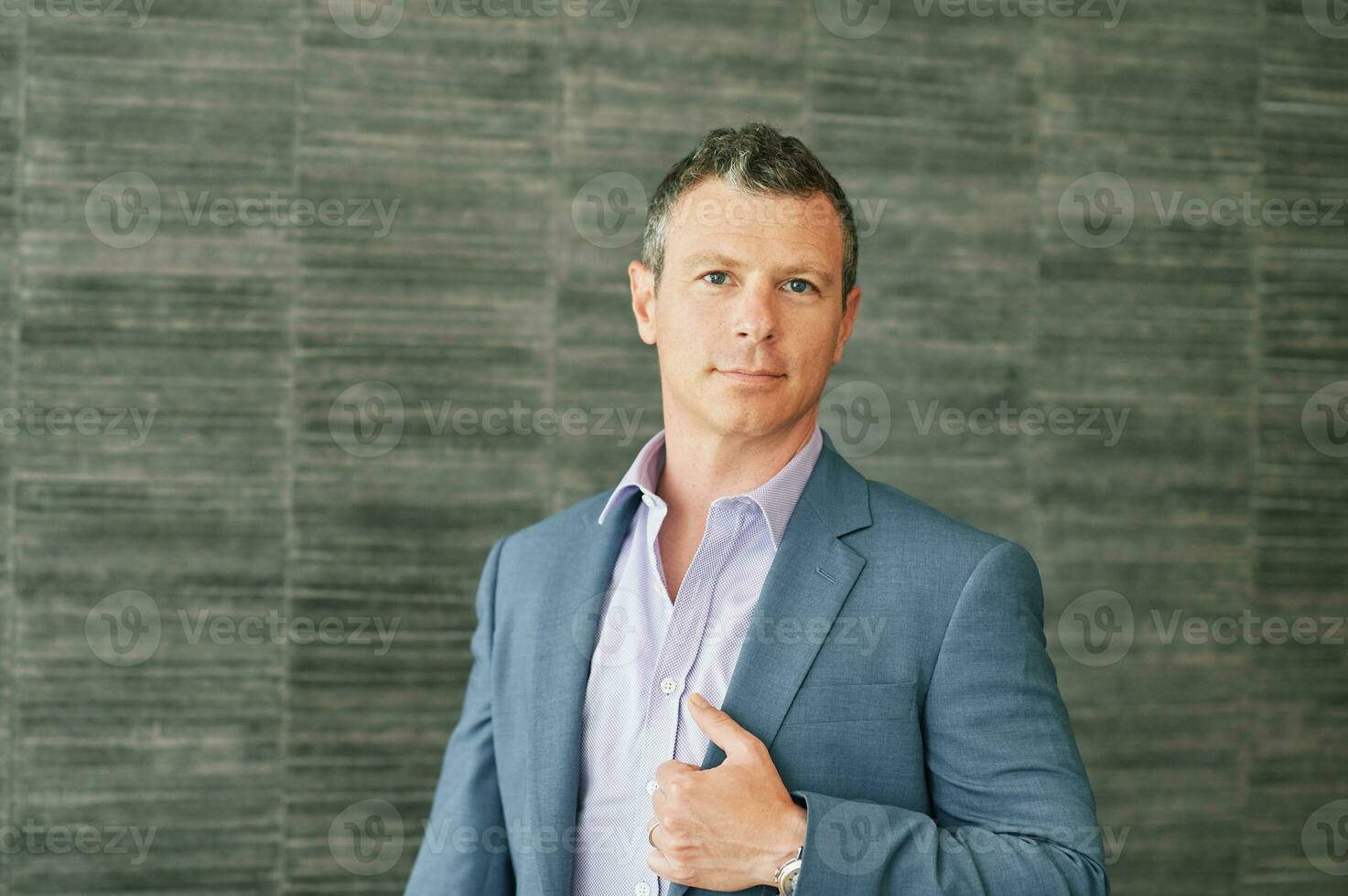 Portrait of mature 40 year old man posing bext to grey wall background, wearing purple shirt and blue jacket photo