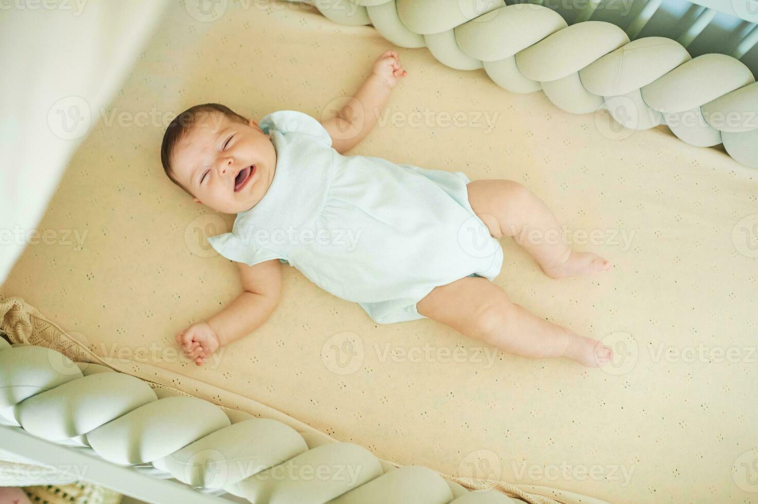 Little crying 6 months old baby lying in a crib, top view photo
