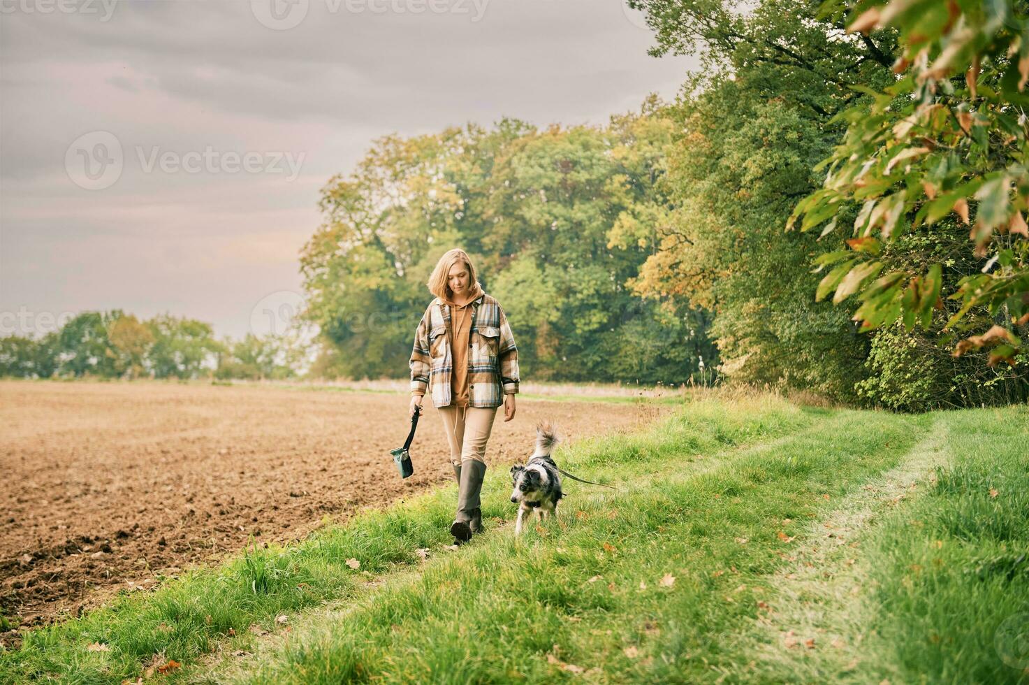 Farm landscape, young woman walking with australian shepherd dog photo