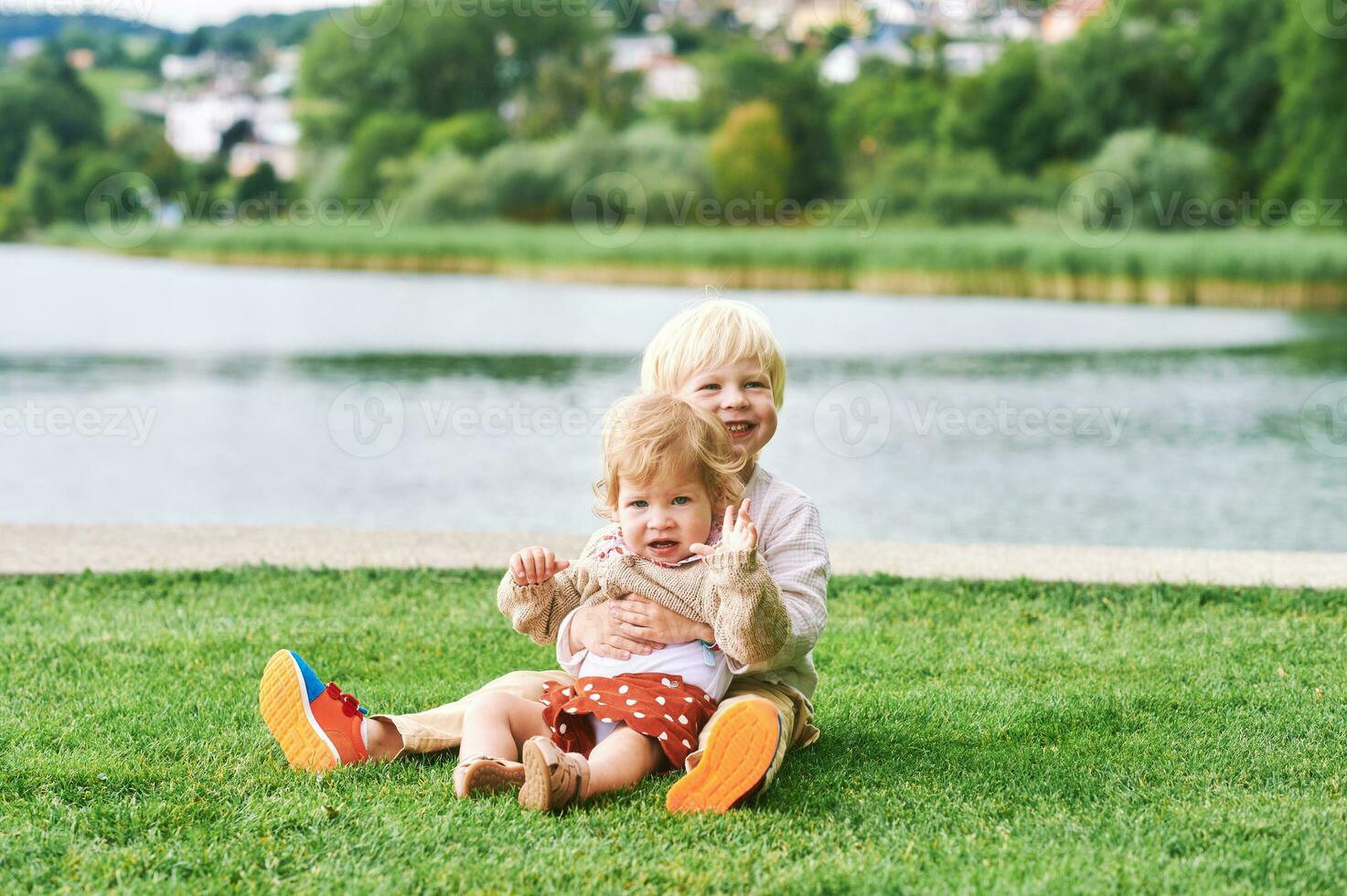 Outdoor portrait of adorable happy children playing together next to lake or river, siblings love photo