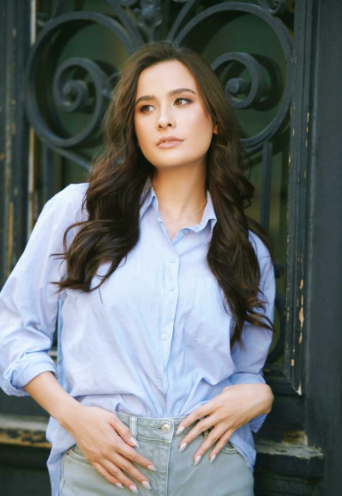 Fashion portrait of beautiful young woman, wearing blue shirt, posing outdoors photo