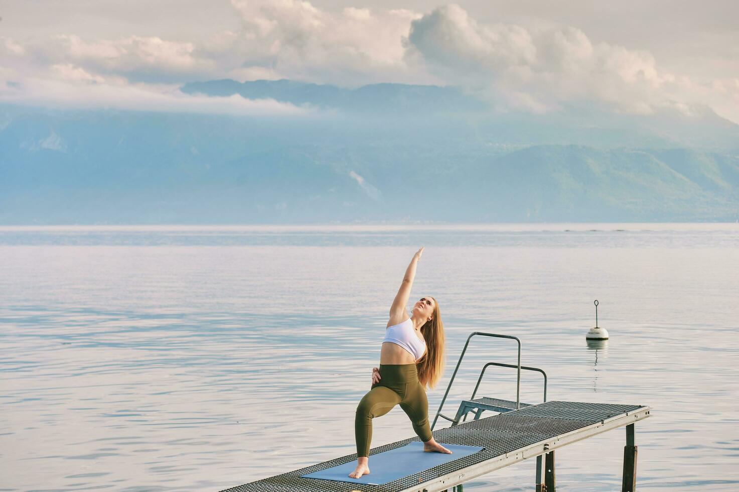 Outdoor portrait of young beautiful woman practicing yoga by the lake photo