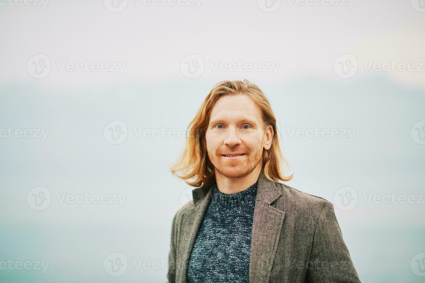 Outdoor portrait of young red haired man, wearing pullover and coat, cold foggy day photo