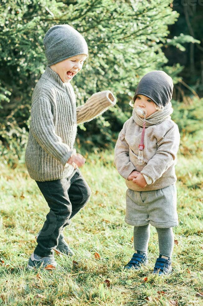 Outdoor portrait of little preschool brother trying to cheer up shy toddler sister photo