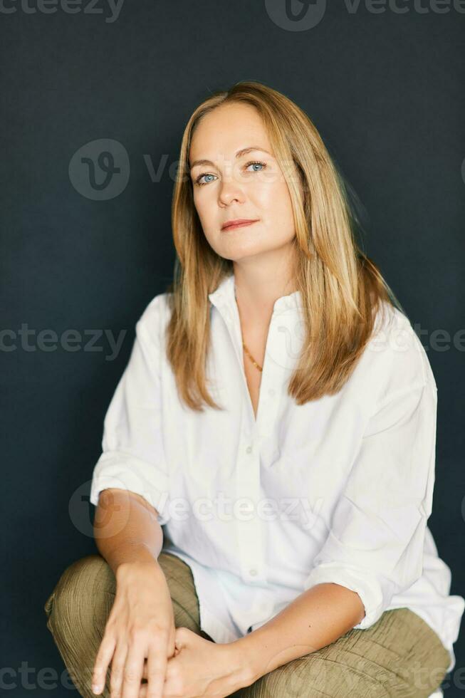 Studio portrait of beautiful confident woman posing on black background, wearing white shirt photo