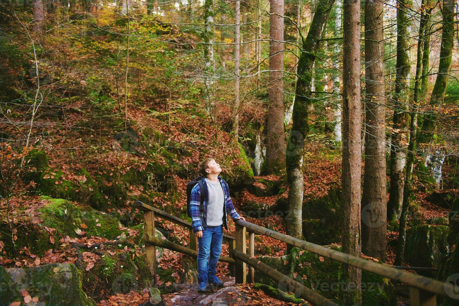 Outdoor portrait of happy kid boy hiking in autumn forest, wearing backpack photo