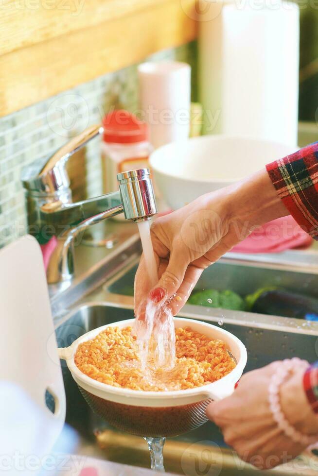 Close up image of female hands washing lentils in colander under running tap water photo