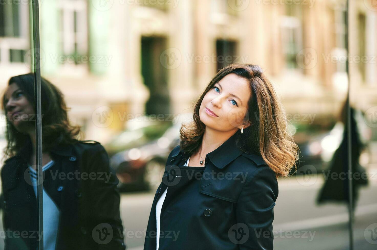 Outdoor portrait of beautiful 40 year old woman leaning on mirror wall, street fashion photo