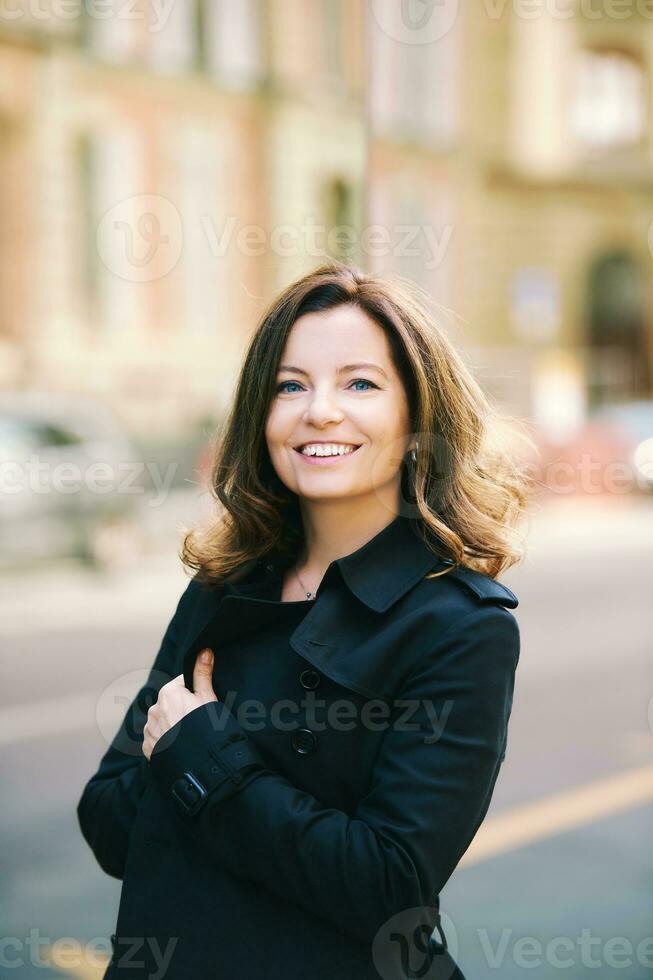 Outdoor portrait of beautiful 40 year old woman leaning on mirror wall, street fashion photo