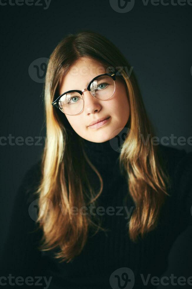 estudio retrato de bonito joven Adolescente niña posando en negro fondo, vistiendo lentes foto