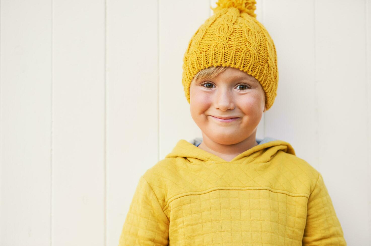 Close up portrait of adorable 5 year old kid wearing yellow sweatshirt and hat, posing on white background photo