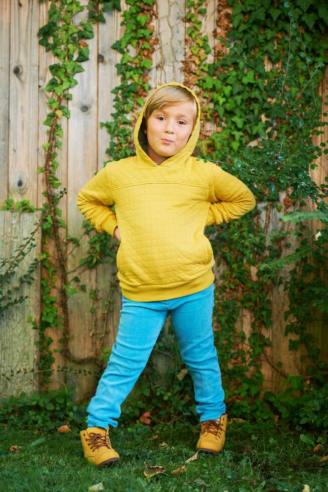 Outdoor portrait of adorable 5 year old boy wearing yellow hoodie and turquoise jeans photo