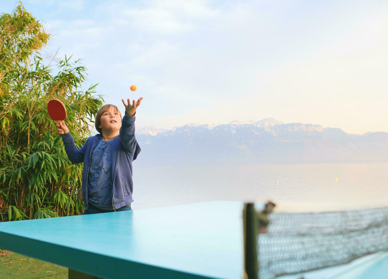 Kid boy playing  ping pong by the lake, active lifestyle for children photo