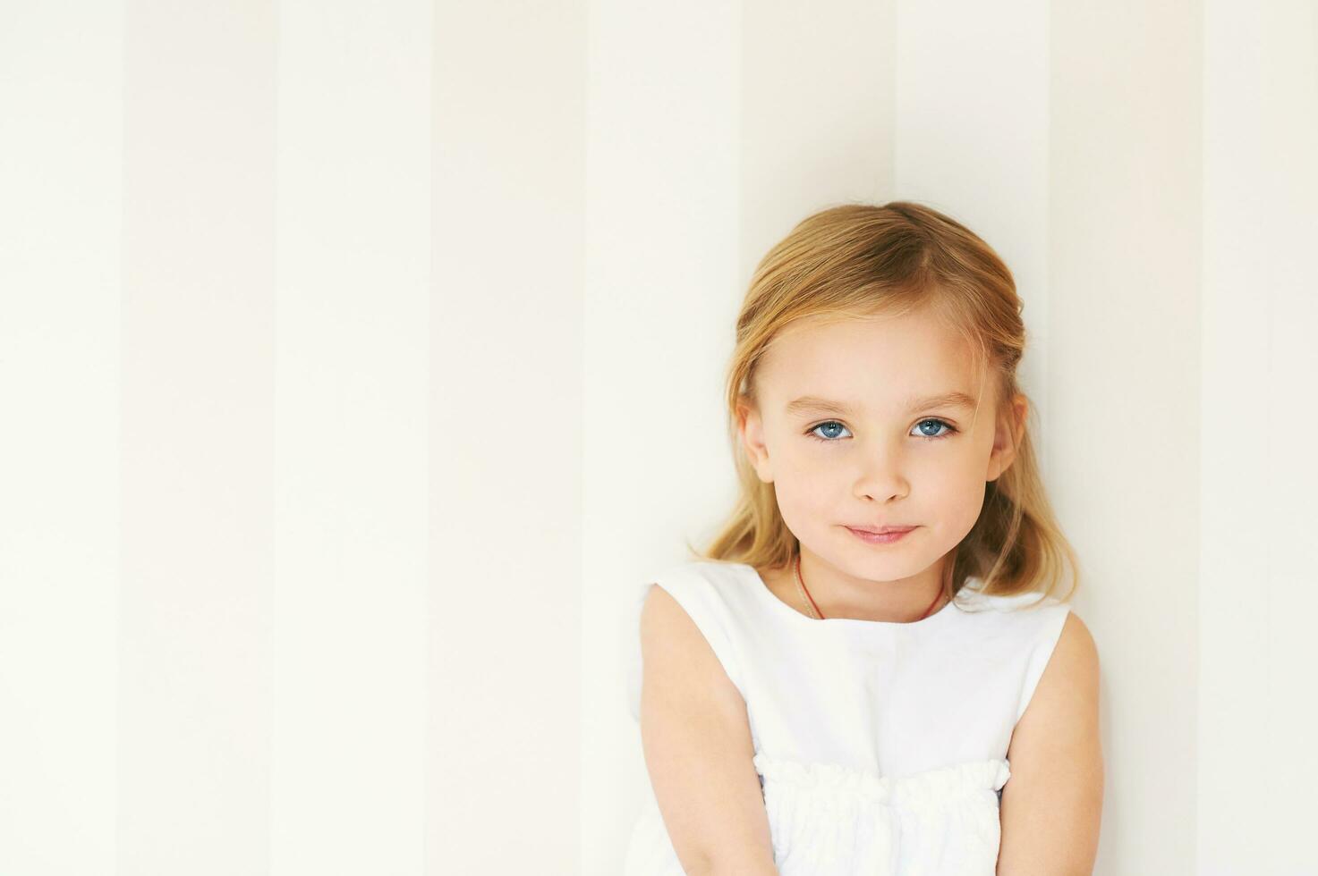 retrato de adorable pequeño niña con azul ojos vistiendo blanco vestir foto