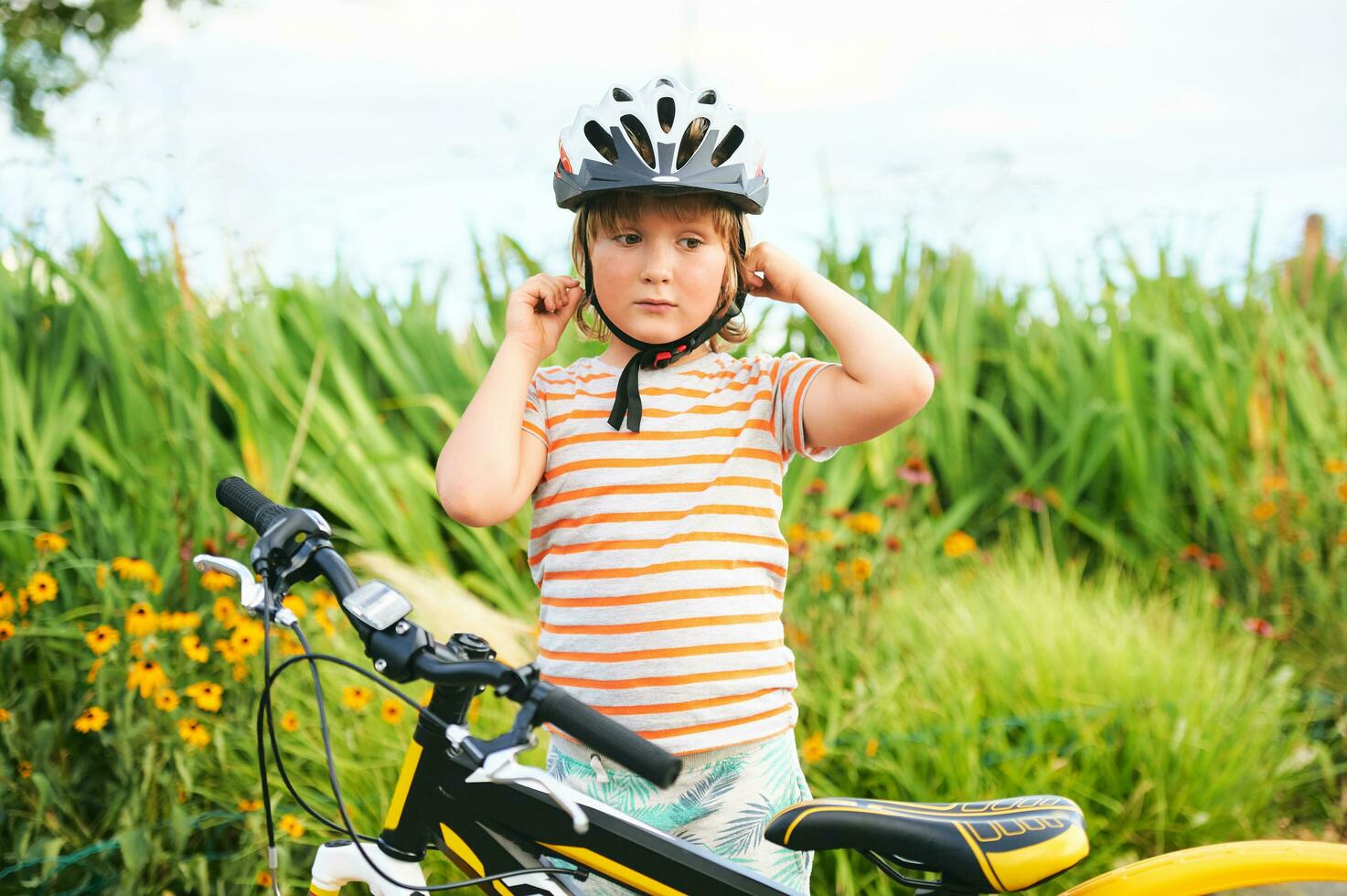 Cute little boy riding bicycle in the park, sport for children, active family outside. Child putting safe helmet photo