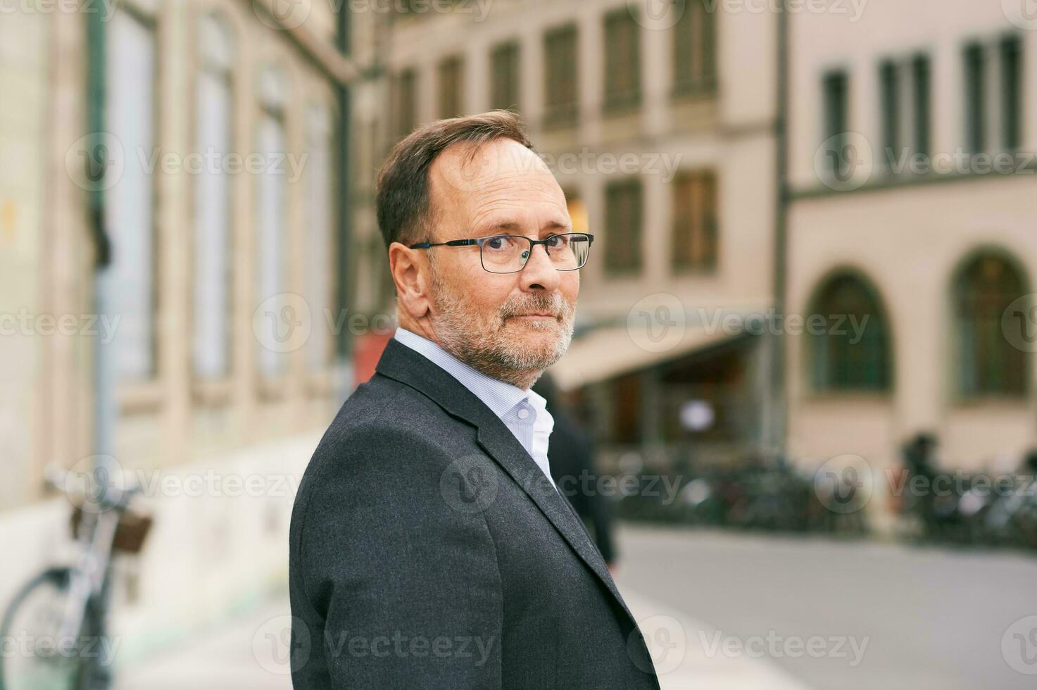 Outdoor portrait of middle age man looking back over the shoulder, wearing glasses and grey suit photo