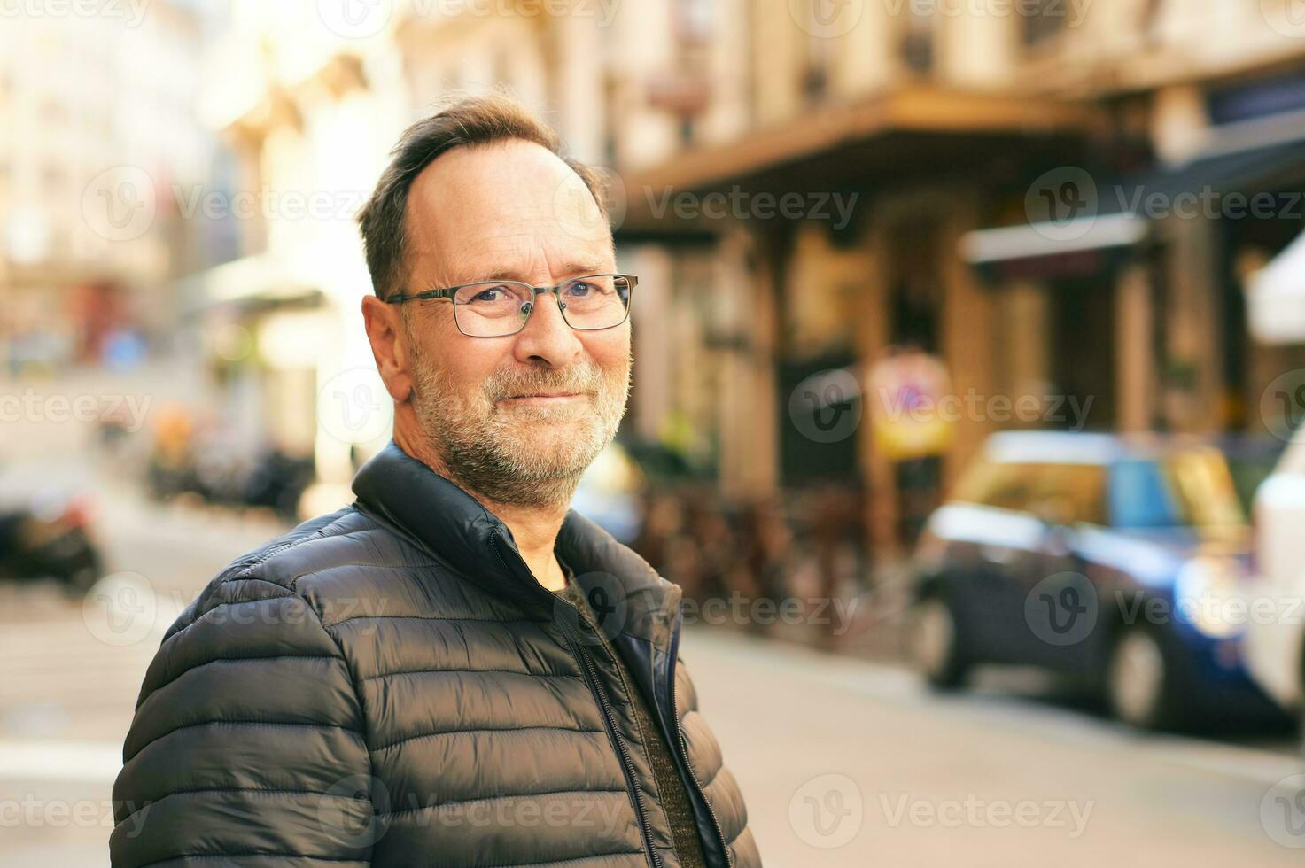 Outdoor portrait of middle age man in city, wearing blue jacket and eyeglasses photo