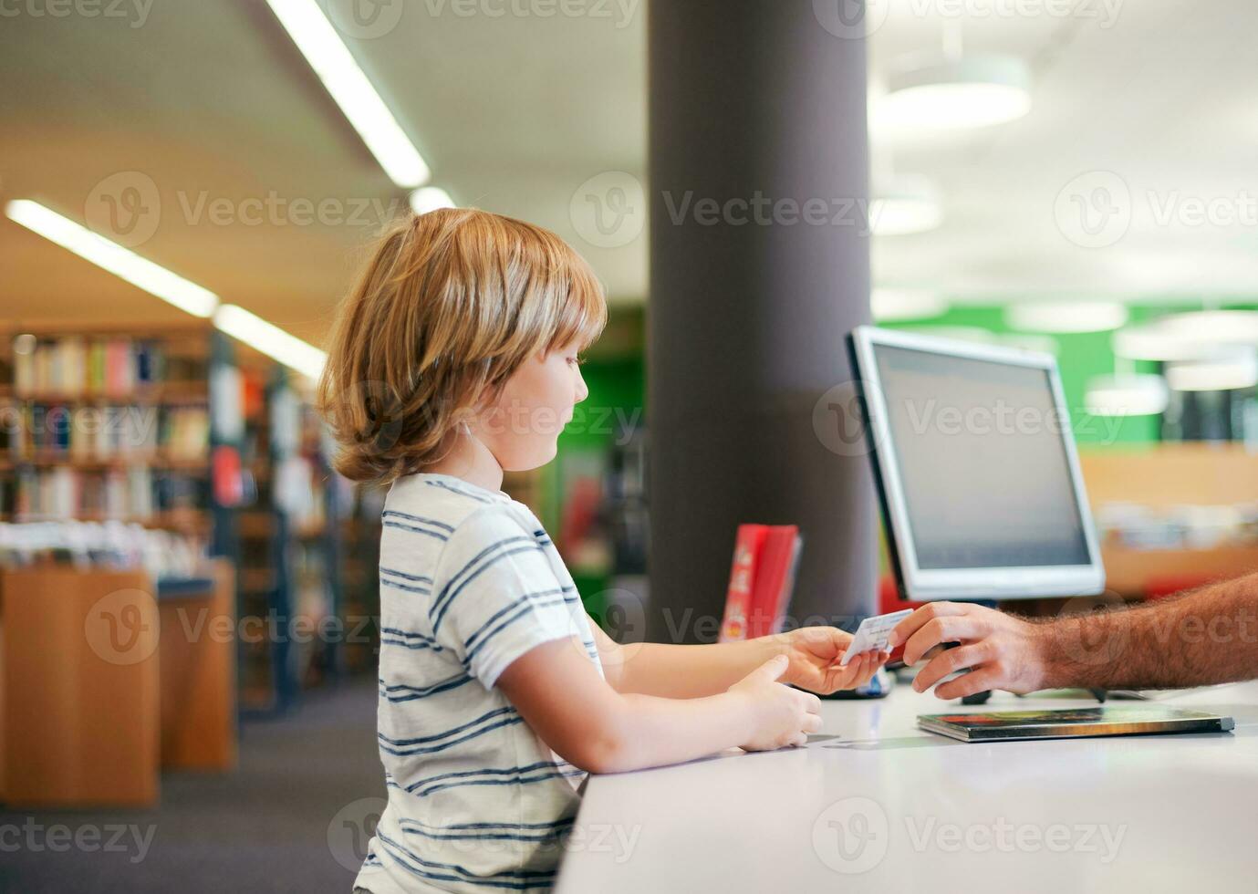 Portrait of cute little boy taking books in library, giving  membership card to librarian photo