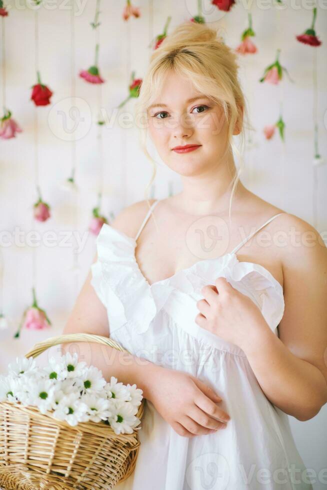 estudio retrato de bonito joven Adolescente 15 - dieciséis año antiguo niña vistiendo verano vestido, posando en blanco antecedentes con colgando rosas, participación cesta con margarita flores, belleza y Moda concepto foto