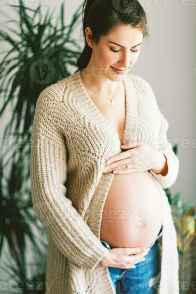 Indoor portrait of happy young pregnant woman wearing warm knitted jacket photo