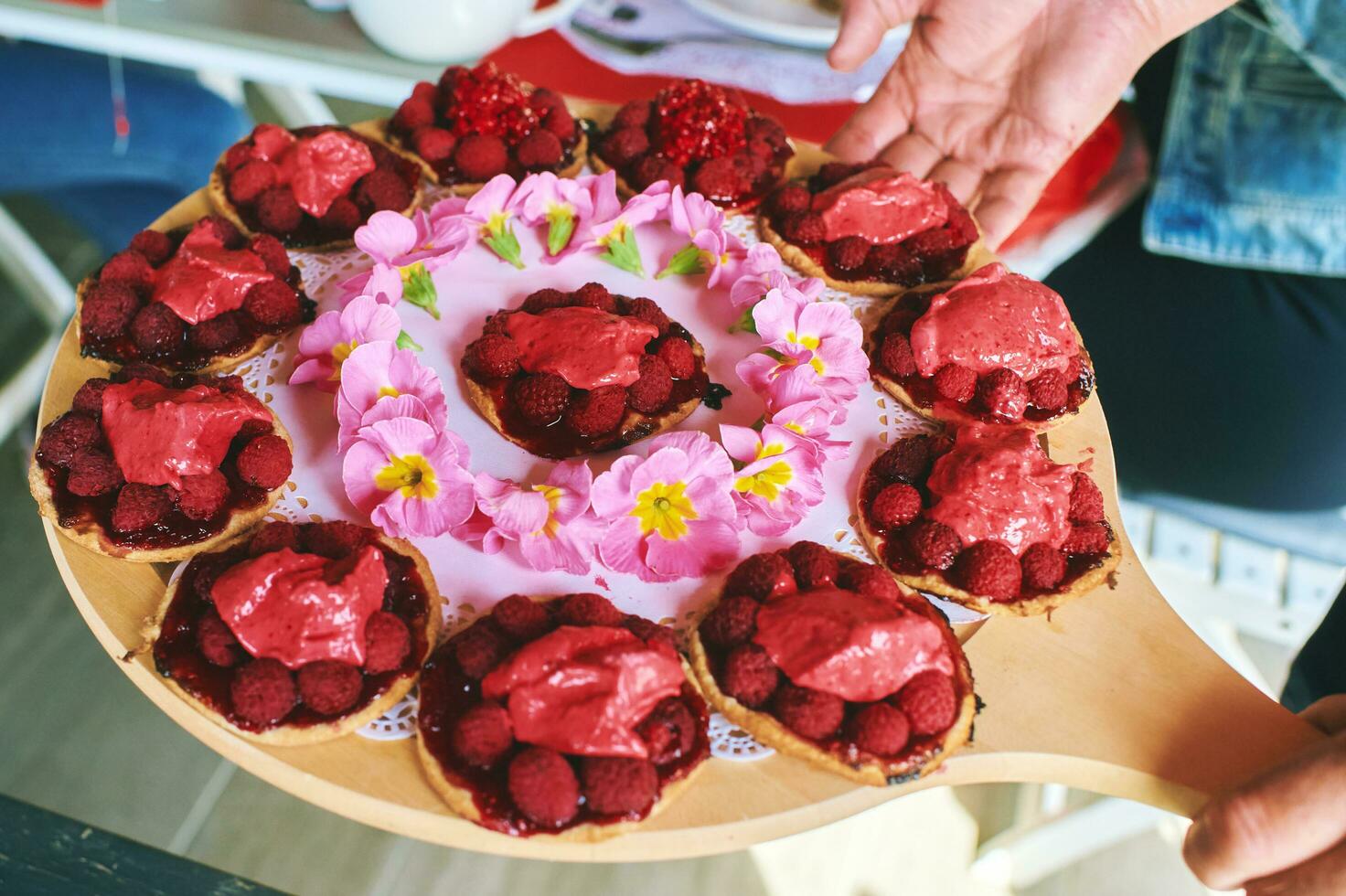 Person holding tray with many fresh fruit pie tart with with raspberries photo