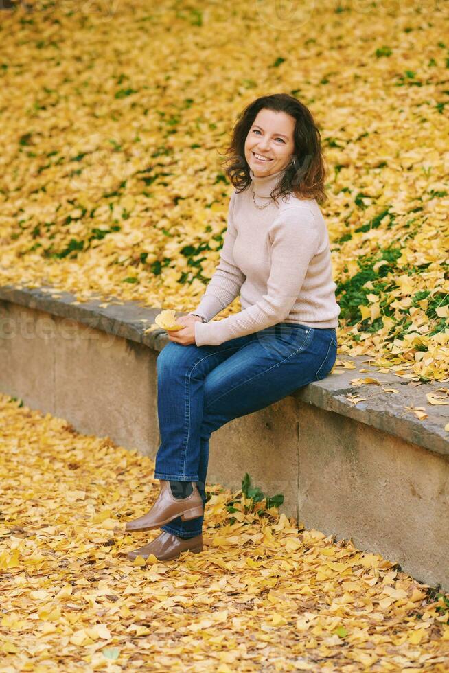 otoño retrato de hermosa maduro mujer, relajante en dorado otoño parque foto