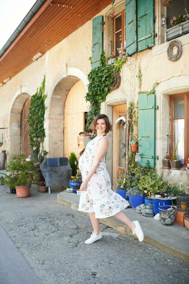 Outdoor portrait of happy young pregnant woman dancing on the street in countryside photo