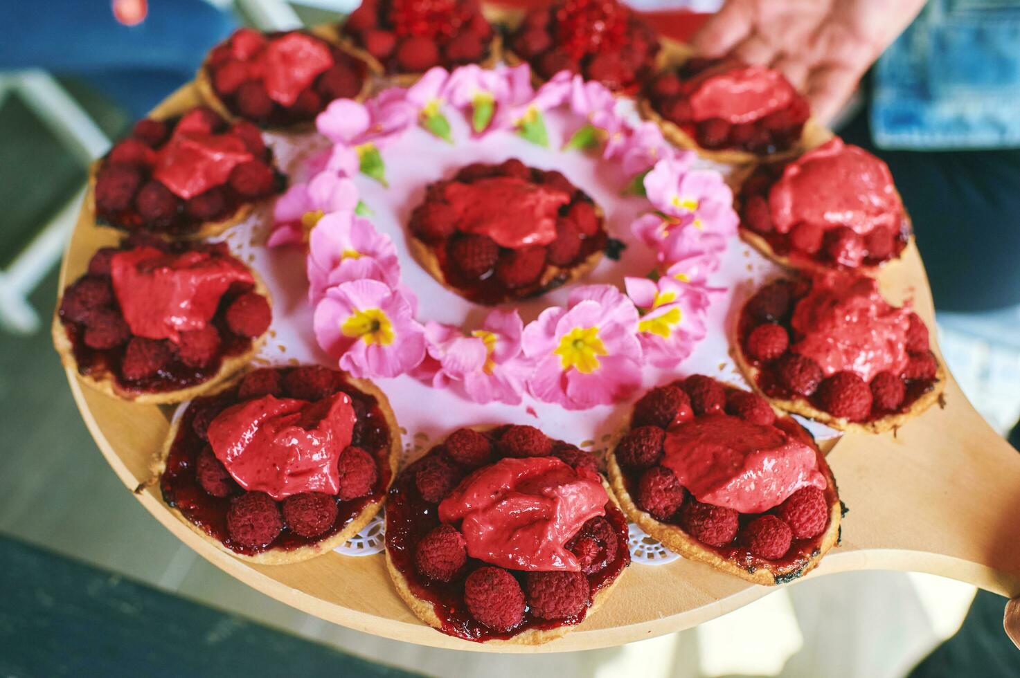 Person holding tray with many fresh fruit pie tart with with raspberries photo