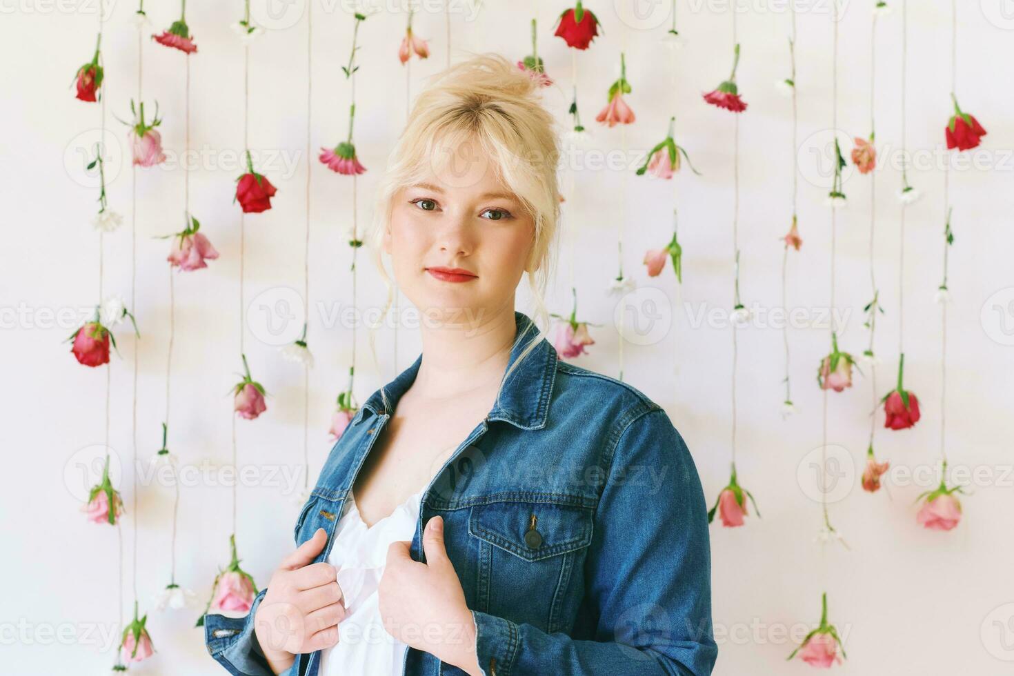 Studio portrait of pretty young teenage 15 - 16 year old girl wearing denim jacket, posing on white background with hanging flowers, beauty and fashion concept photo