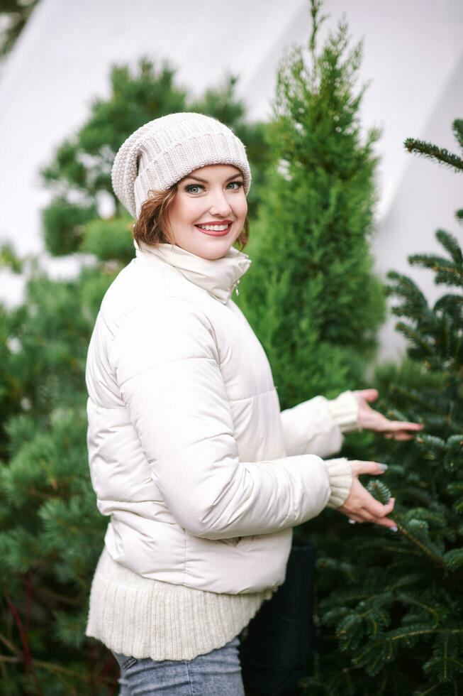 Outdoor portrait of happy young woman choosing christmas tree at market photo