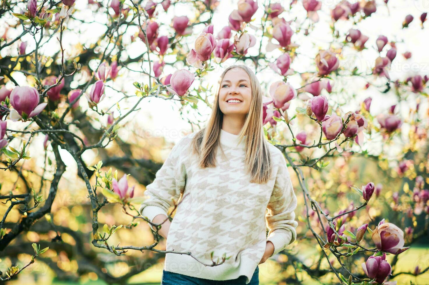 Outdoor portrait of beautiful happy model with blond hair posing next to magnolia flowers photo