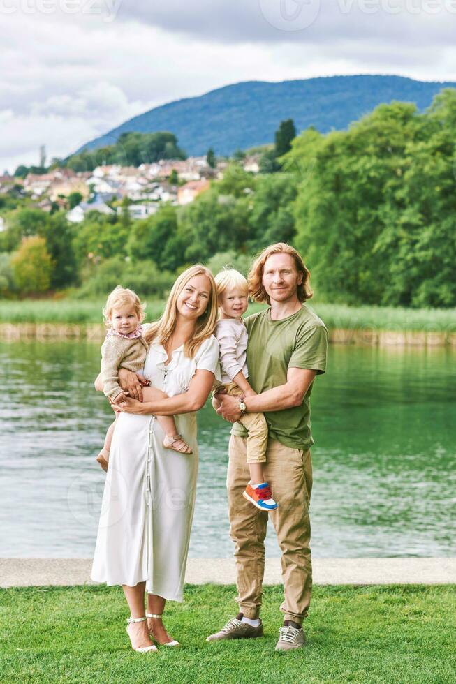 al aire libre retrato de hermosa familia, joven Pareja con preescolar chico y niñito niña posando siguiente a lago o río foto