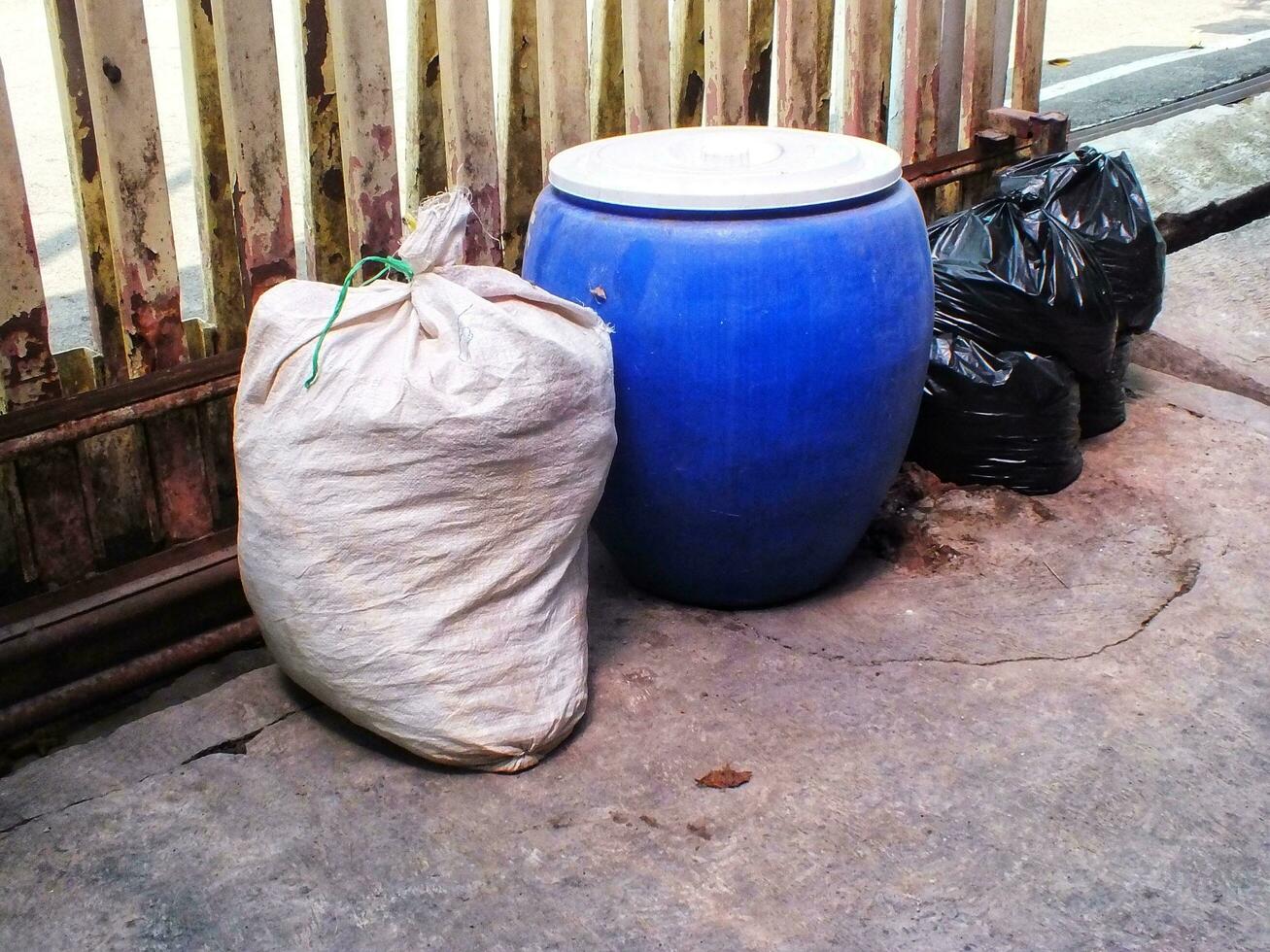 Black plastic bags of rubbish pile beside an old rusty french. Pile of black garbage on the footpath at side road in big city, pollution trash photo