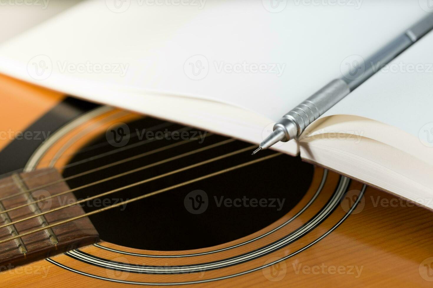 A brown pencil and a dark red notebook are placed on an acoustic guitar. photo