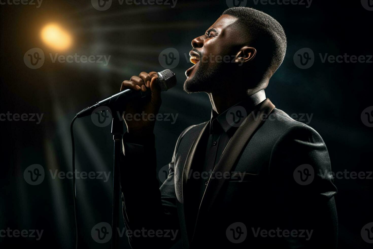 black male singer singing with microphone in front of dark background bokeh style background photo