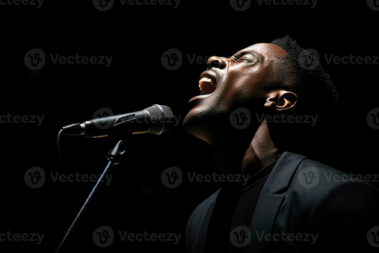 black male singer singing with microphone in front of dark background bokeh style background photo