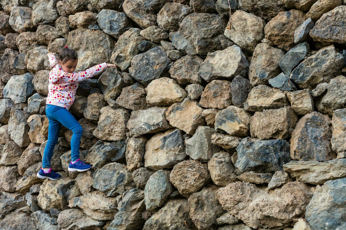 A young girl climbs over the rocks on top of a hill photo