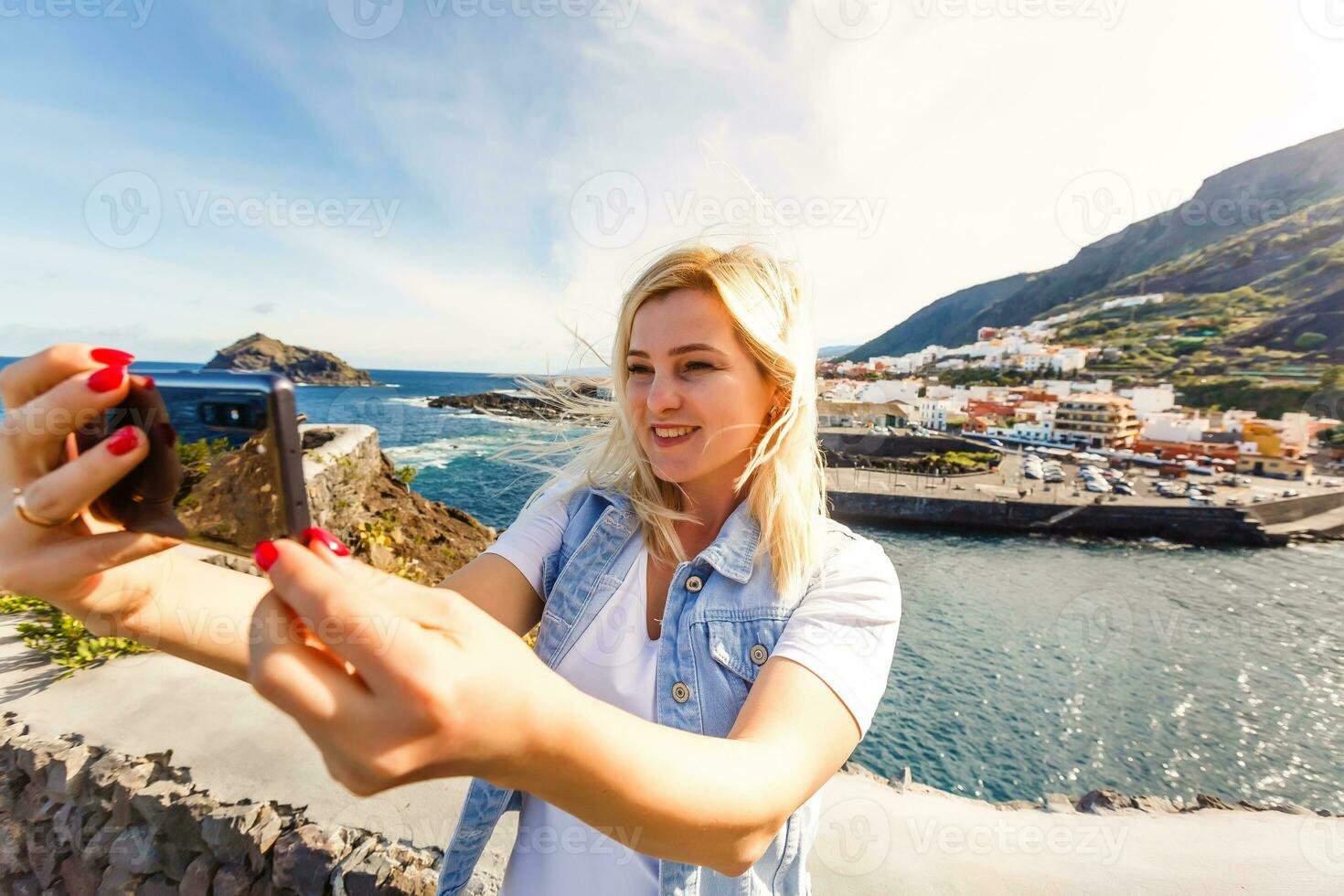 Young girl smiling and speaking consulting and giving instruction with voice recognition. Woman with audio recording in smart phone in the seaside in Garachico, Tenerife photo