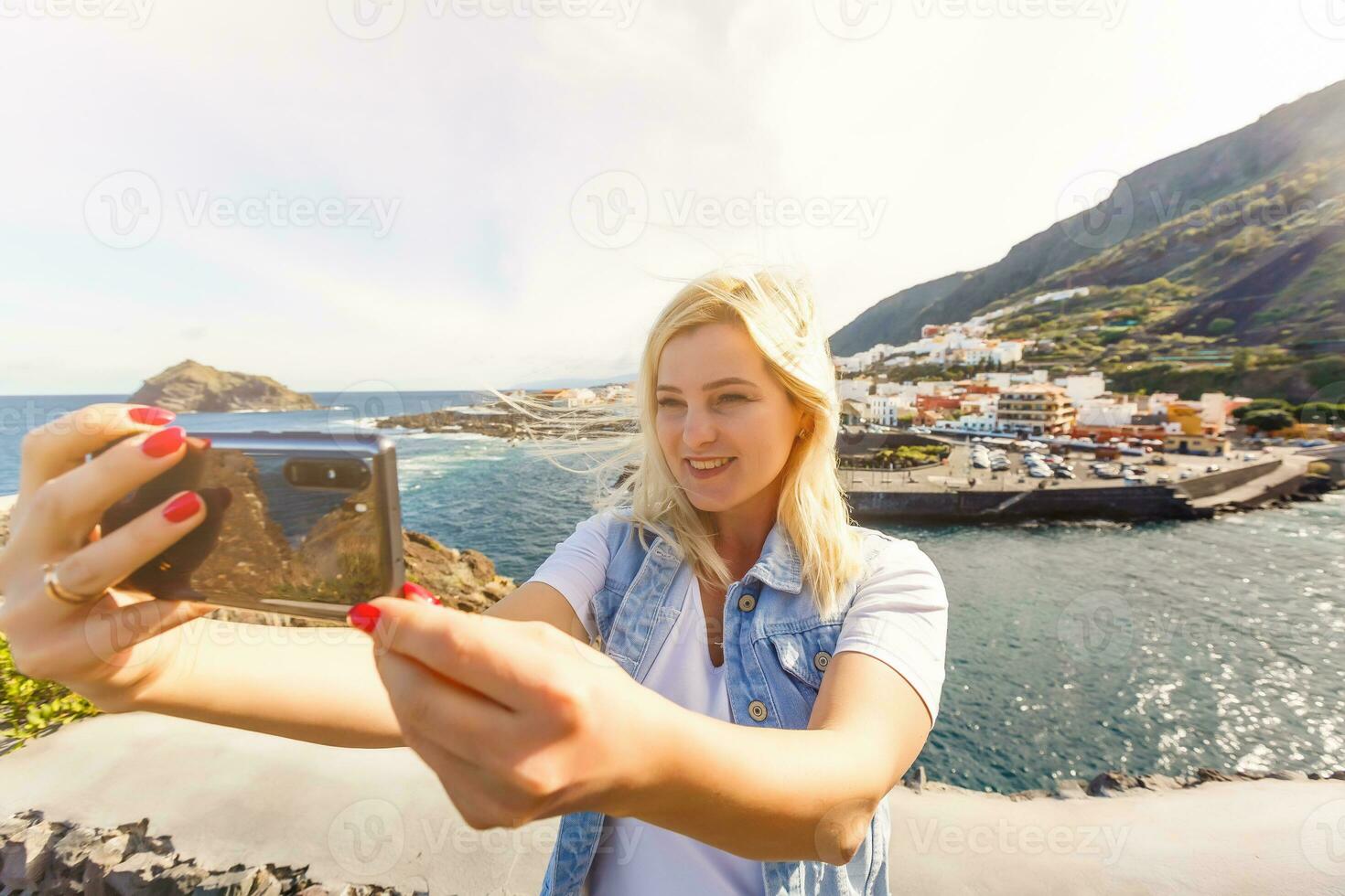 Young girl smiling and speaking consulting and giving instruction with voice recognition. Woman with audio recording in smart phone in the seaside in Garachico, Tenerife photo