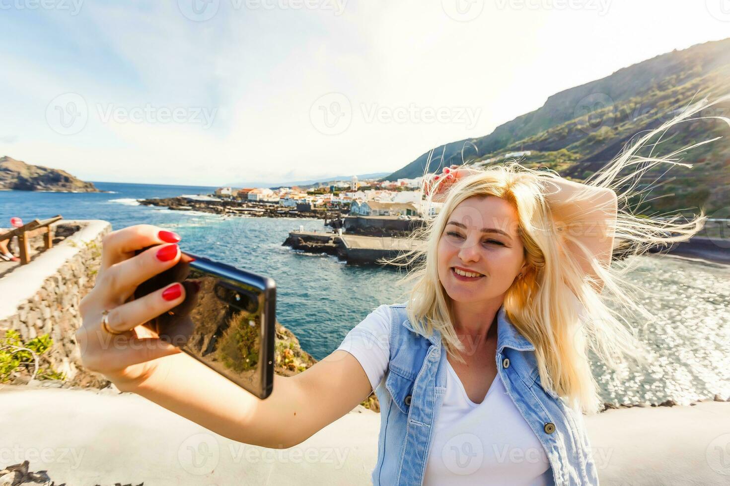 Young girl smiling and speaking consulting and giving instruction with voice recognition. Woman with audio recording in smart phone in the seaside in Garachico, Tenerife photo
