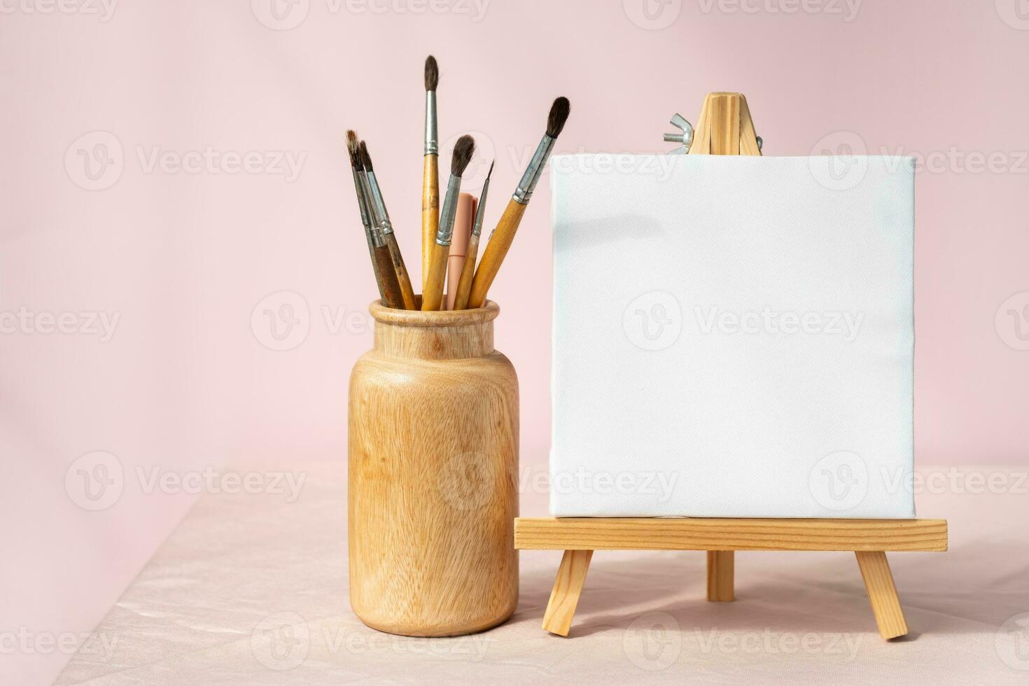 Easel with blank canvas and vase with brushes. Artistic still life. photo