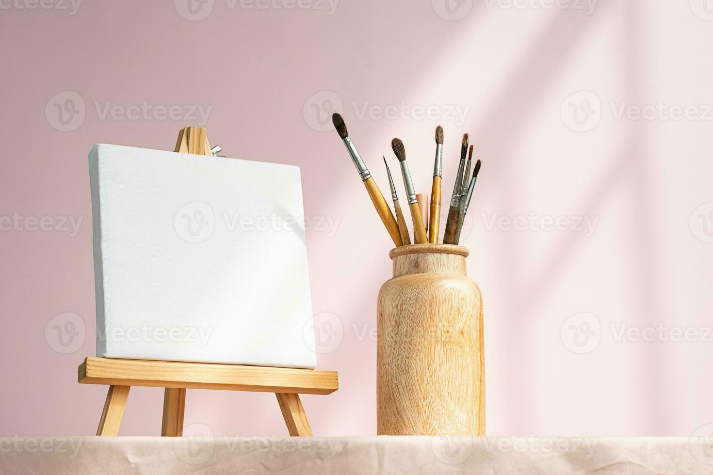 Easel with blank canvas and vase with brushes. Artistic still life. photo