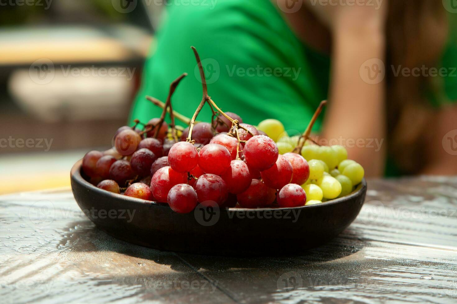 plato de rojo y verde uvas en un de madera mesa y en el antecedentes fuera de atención foto