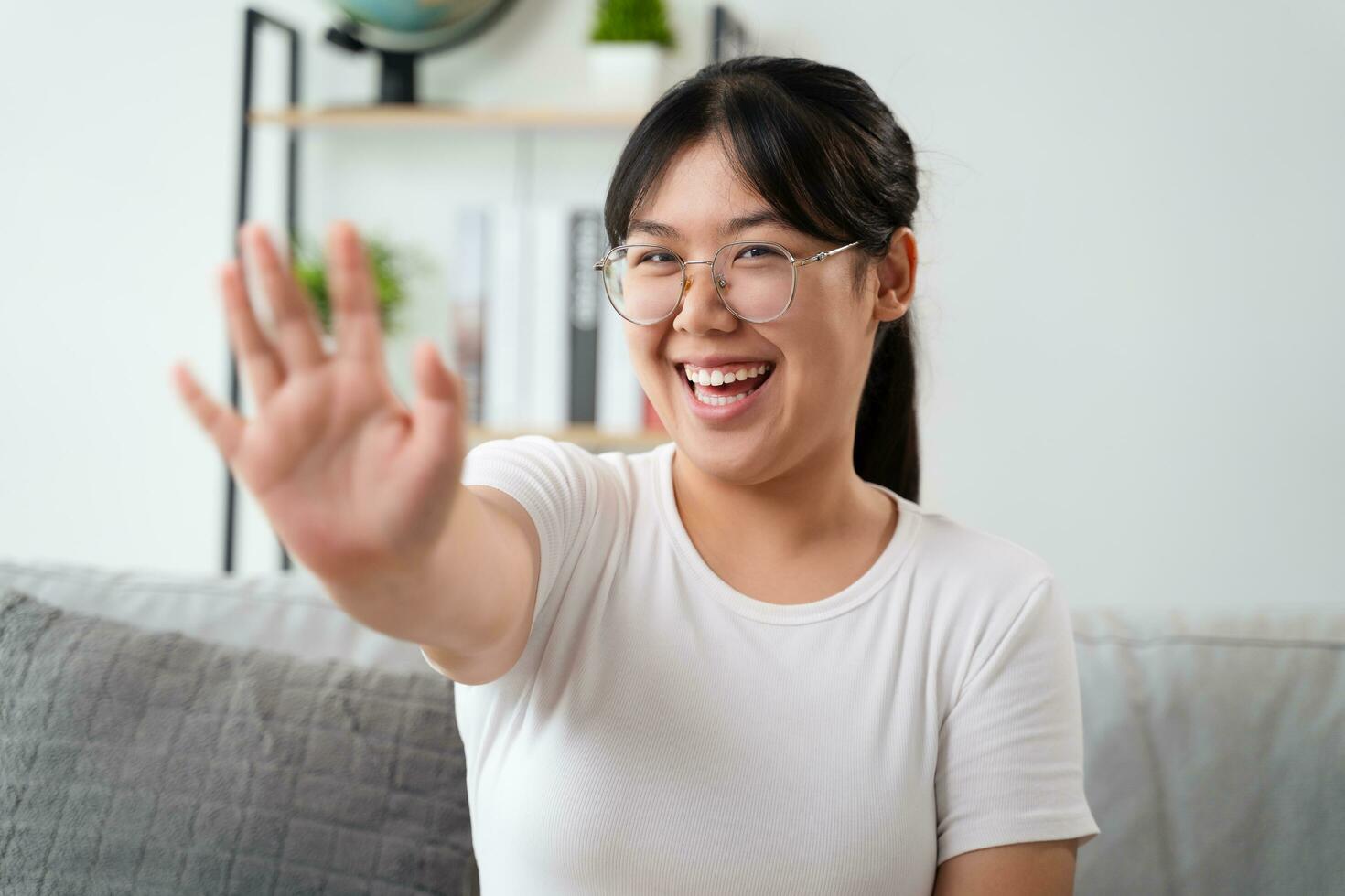 Portrait of young Asian woman wearing eye glasses big smiling and looking at camera with feeling happy and positive in living room at home, meeting, video conference. photo