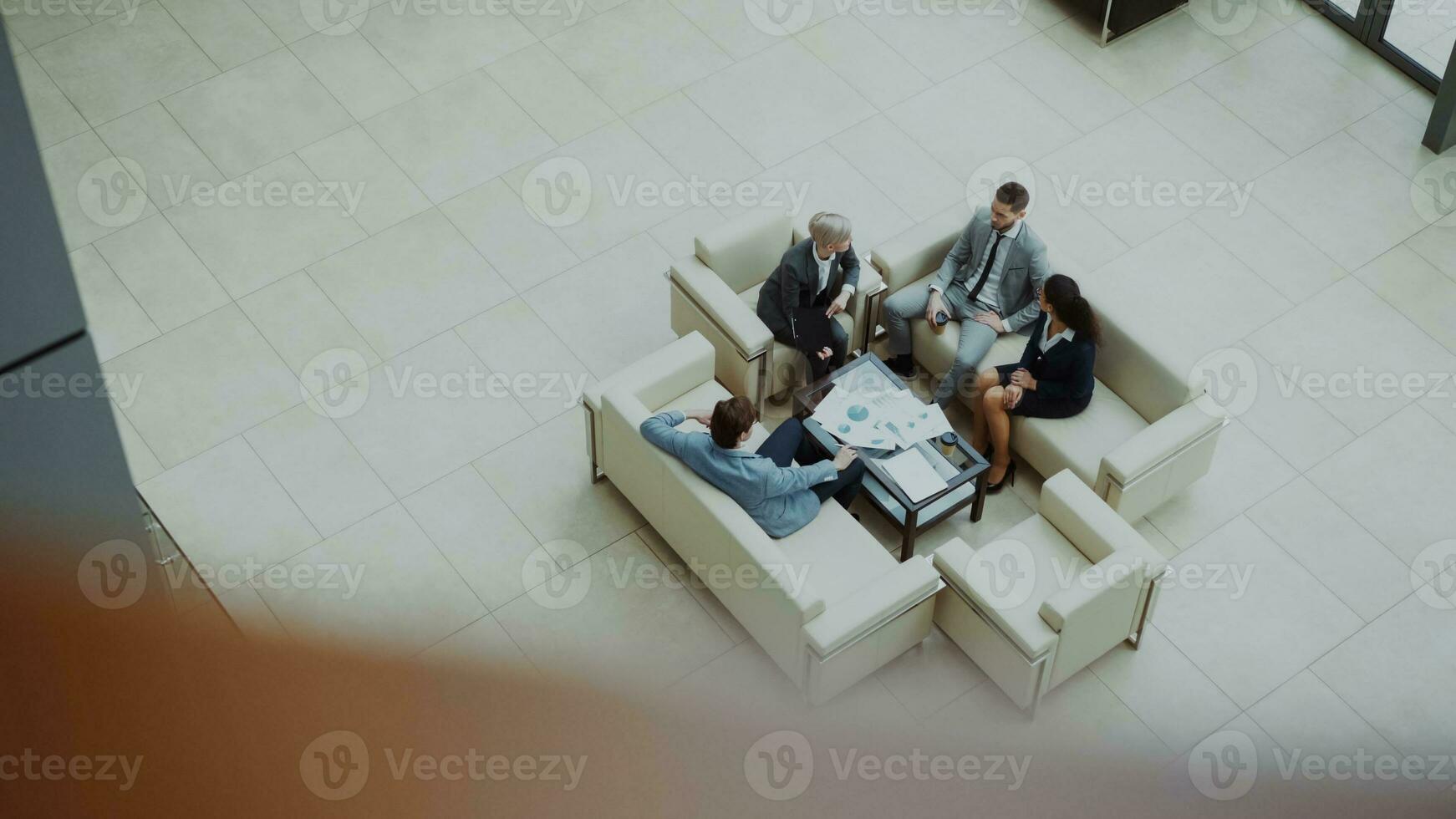 Top view of group of business people colleagues discussing financial charts sitting on couchs in lobby at modern business center indoors photo