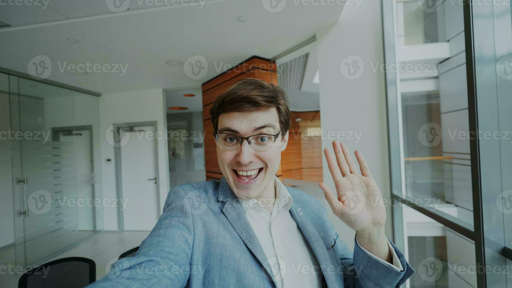 POV of young businessman in suit having online video chat using smartphone camera and talking to his colleagues in modern office indoors photo