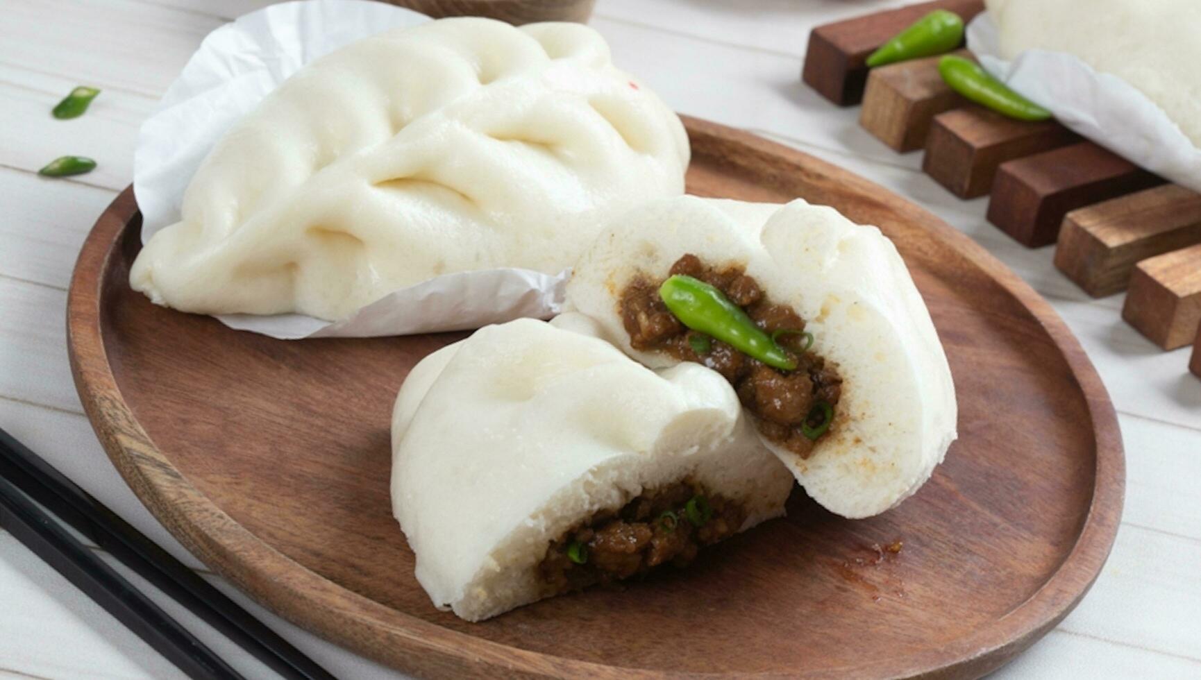 chino alimento, baozi es un tradicional delicadeza en porcelana, un pan comida fotografía entonces tentador, delicioso baozi, chino al vapor carne bollo es Listo a comer en servicio plato y buque de vapor foto